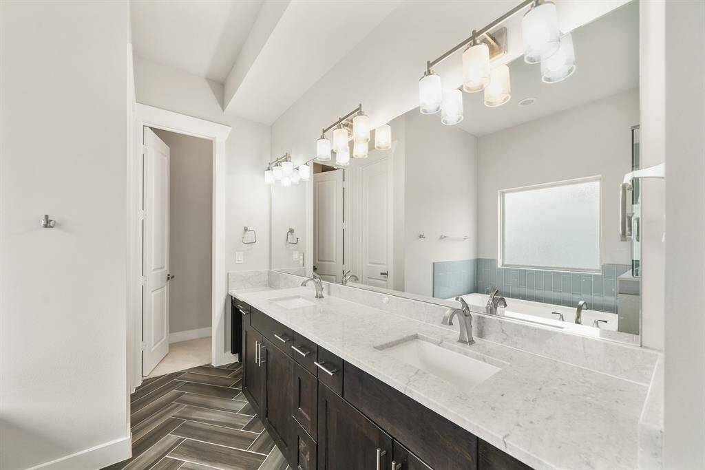 Wood-stained Shaker-style cabinetry supports an extended quartz surfaced counter top with integrated back splash and includes dual under-mount sinks and a make-up vanity area with wall mounted mirror & lighting above.
