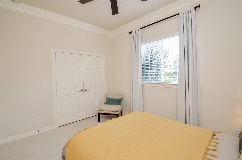 On the other side of the living room in this split floorplan, this secondary bedroom features neutral walls in Sherwin Williams Casa Blanca, new carpet (2024) a large window with drapes, a new ceiling fan (2023), and a French door closet.