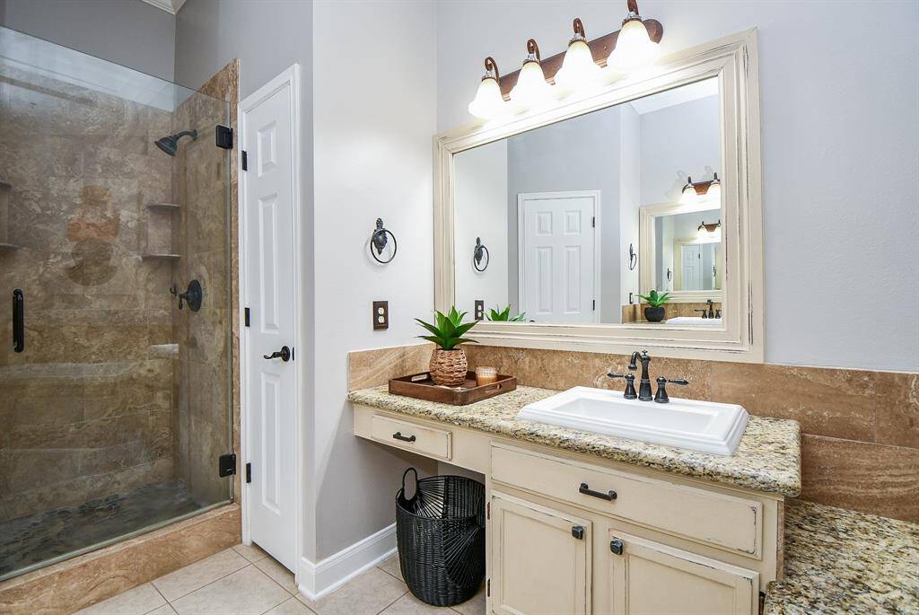 Remodeled primary bathroom with double sinks and stand up shower with rock flooring.
