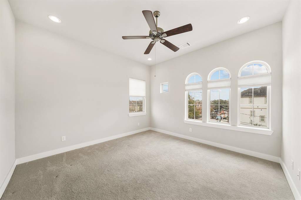 The secondary bedroom complete with an en-suite bath has a high ceiling with recessed lighting and ceiling fan with light fixture, arched windows with shades overlooking the front yard & carpet.