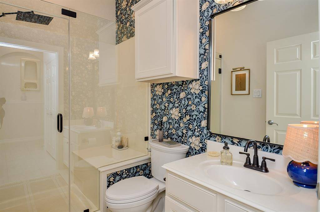 This secondary bathroom is stylish, featuring a floral wallpaper accent, a new glass-enclosed shower, and a single vanity with a new Moen faucet. The new American Standard toilet was replaced in 2023.