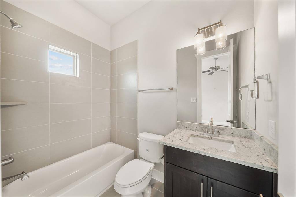 Serving as the home's second full bath, features include wood-stained cabinetry with a granite counter top & under-mount sink, wall mounted mirror & lighting, a ceramic tile surrounded combination tub/shower with window above & tile flooring.