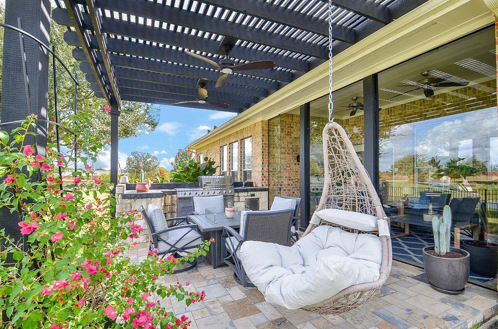 This inviting outdoor space features a covered patio with a pergola, comfortable seating, a hanging chair, and a built-in grill area. It's perfect for entertaining or relaxing, with lush greenery and views of the surrounding landscape.