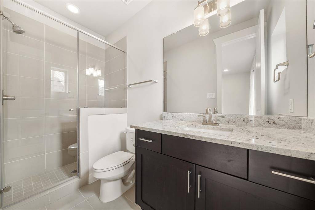 Featuring a beautiful tile surrounded & glass enclosed walk-in shower with recessed lighting above, this third full bath includes wood-stained cabinetry with a granite counter & under-mount sink highlighted by a wall mounted mirror with lighting above & tile flooring.