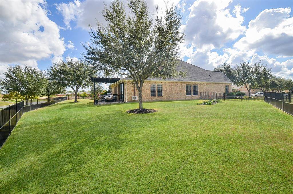 Spacious backyard with well-maintained lawn, mature trees, and a covered patio area, perfect for outdoor relaxation. The property is bordered by a secure black metal fence, installed in 2023.  The HOA installs new iron fencing every 15 years.