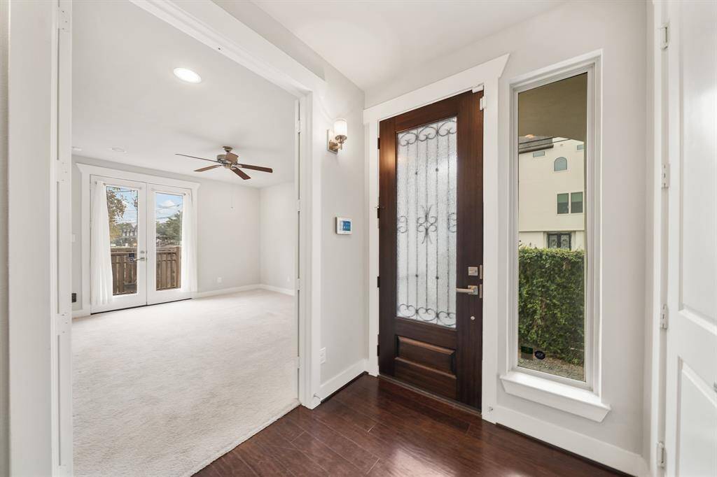 Included is a wood-stained front door with rain privacy glass & wrought iron accents illuminated by wall sconce lighting. A large window offers views of the landscaped side yard and the double door entry on the left leads to the first floor bedroom.