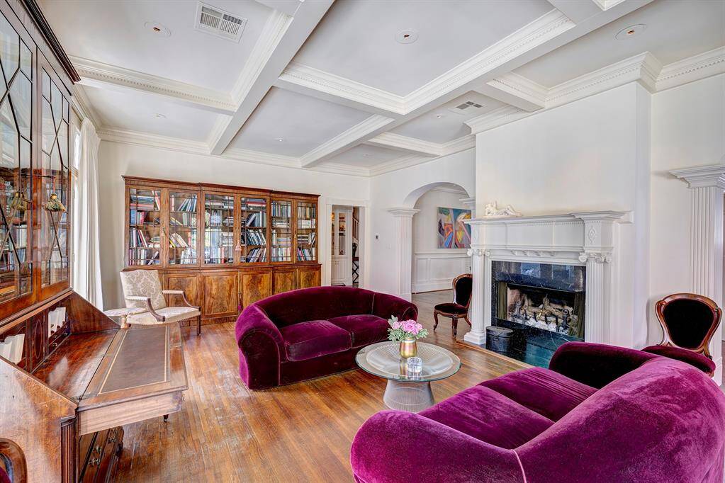 Elegant living room with a classic fireplace as its centerpiece. The fireplace boasts a beautifully carved wooden mantle, adding charm and character to the space. Polished original wood floors complement the warm tones.