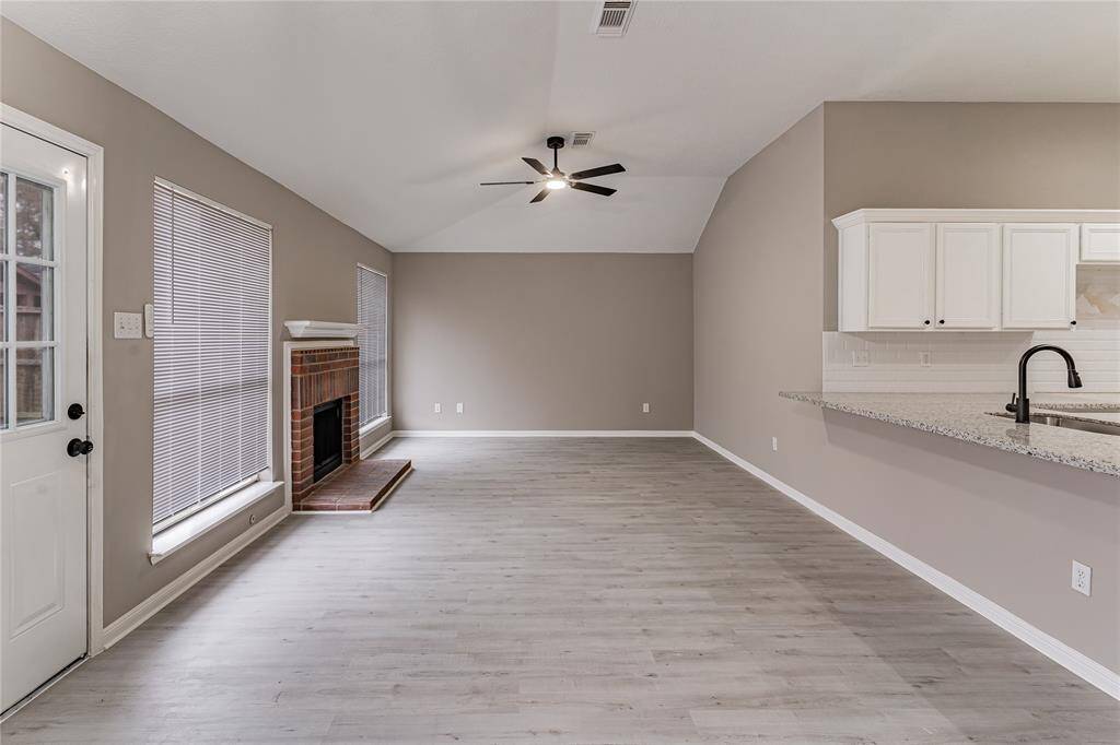 Bright and spacious living area featuring modern flooring, a cozy brick fireplace, and an open layout perfect for entertaining.