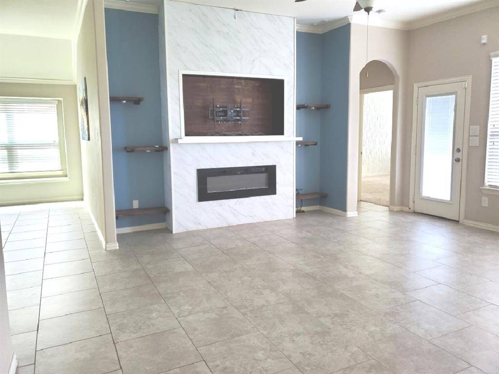 This living room features a spacious and modern design. It has a sleek fireplace, complemented by built-in shelves. Large windows provide ample natural light, and the ceiling fan adds comfort.