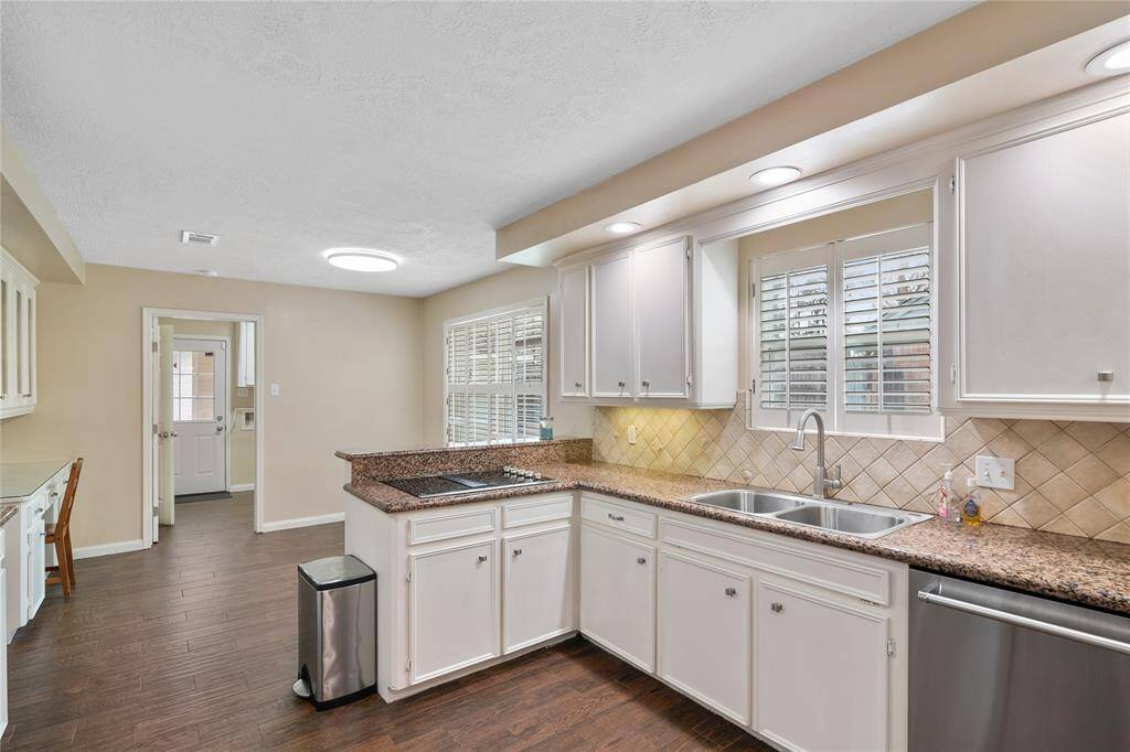 This kitchen features granite countertops, white cabinetry, and stainless steel appliances. It has a double sink under a window with ample natural light, and the space is enhanced by tile flooring.