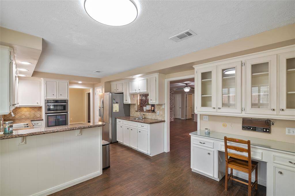 This kitchen features a spacious design with granite countertops and ample cabinet space. It includes modern appliances, a built-in desk area, and a cozy breakfast bar.