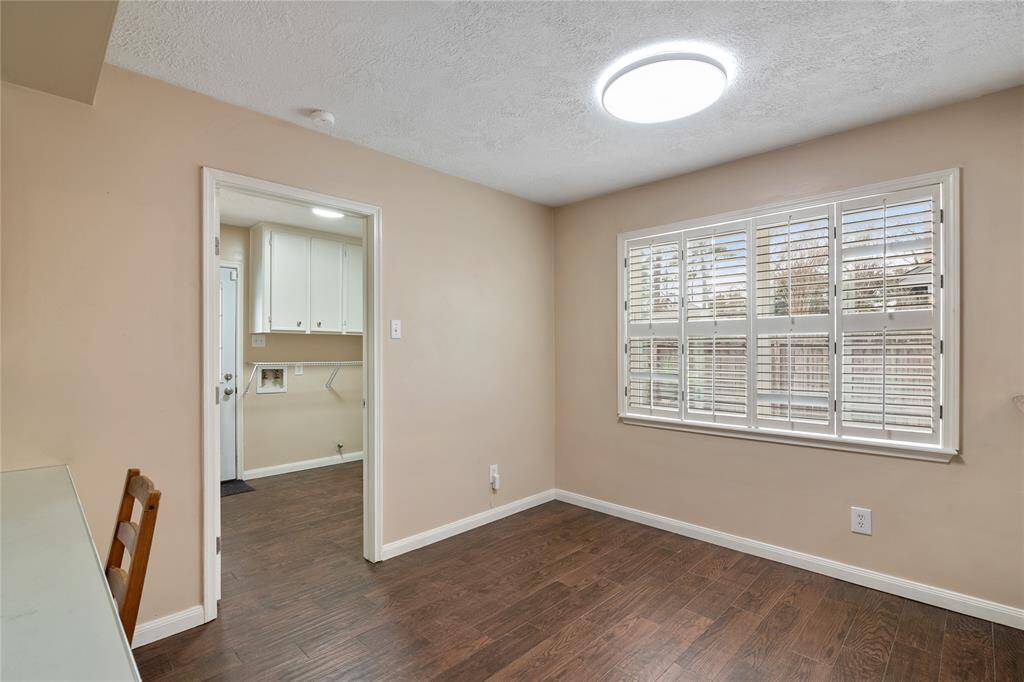 This breakfast room features warm beige walls, tile flooring, and a large window with shutters allowing natural light. It connects to a utility area with white cabinetry, ideal for a cozy office or sitting area.