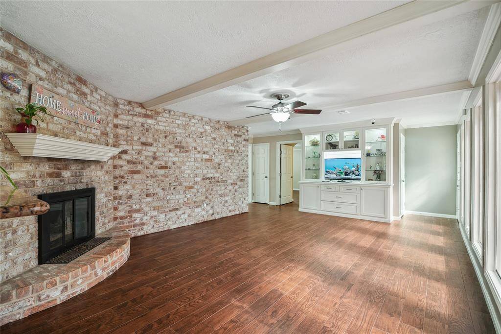 This spacious family room features a cozy brick fireplace, tile floors, built-in shelving and a TV nook, creating a welcoming and functional space.