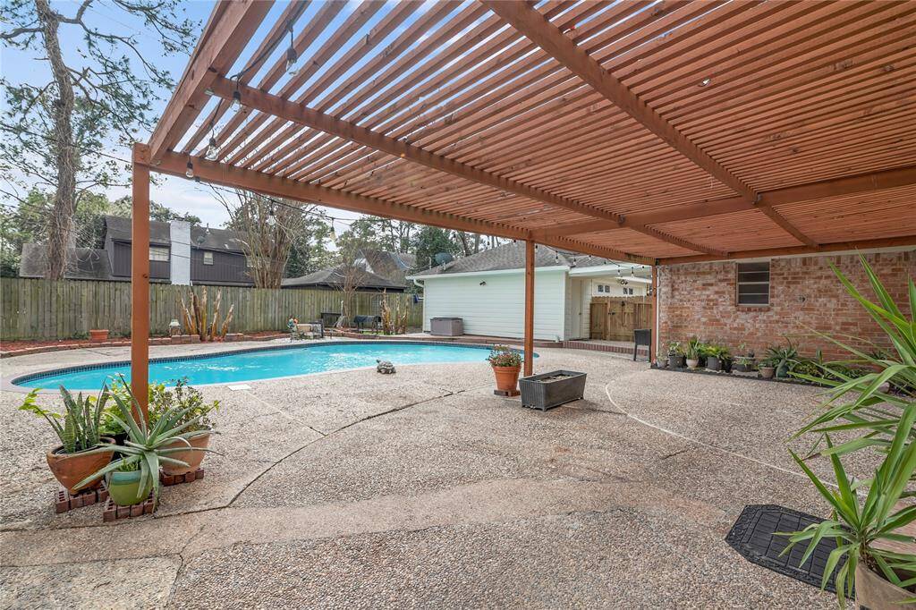 Large patio area with wooden pergola providing shade and in-ground swimming pool.