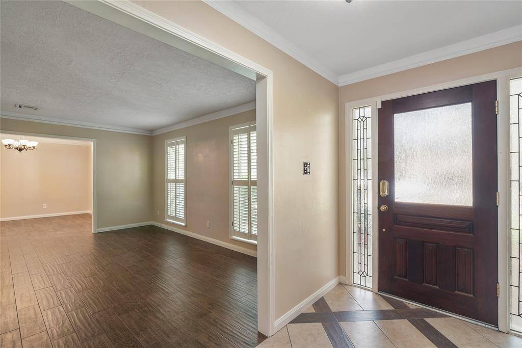 A welcoming entryway with a wooden front door featuring decorative glass panels, and a view of the living room.