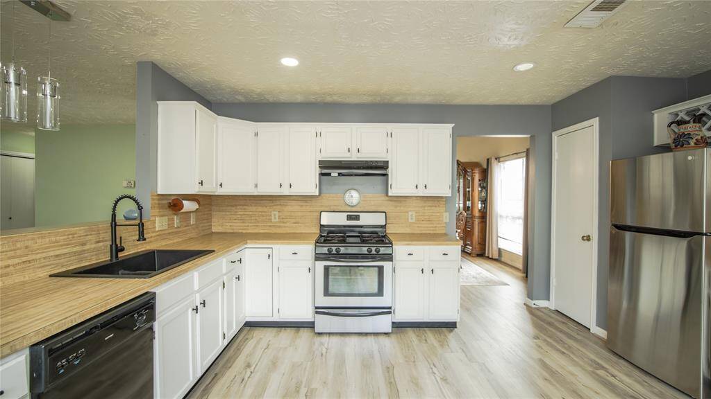 This kitchen features modern appliances, white cabinetry, and wood-look flooring. It has a spacious layout with a sleek black sink, stainless steel refrigerator, and a gas stove, all complemented by neutral walls and ample natural light.