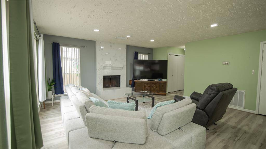 The spacious living room features an updated gas fireplace, light wood flooring, and in-ceiling lighting. Soft green and blue accents enhance the room's charm, while ample natural light creates a bright and inviting atmosphere. Conveniently located adjacent to the living room are the utility room and guest bathrooms, offering easy access.