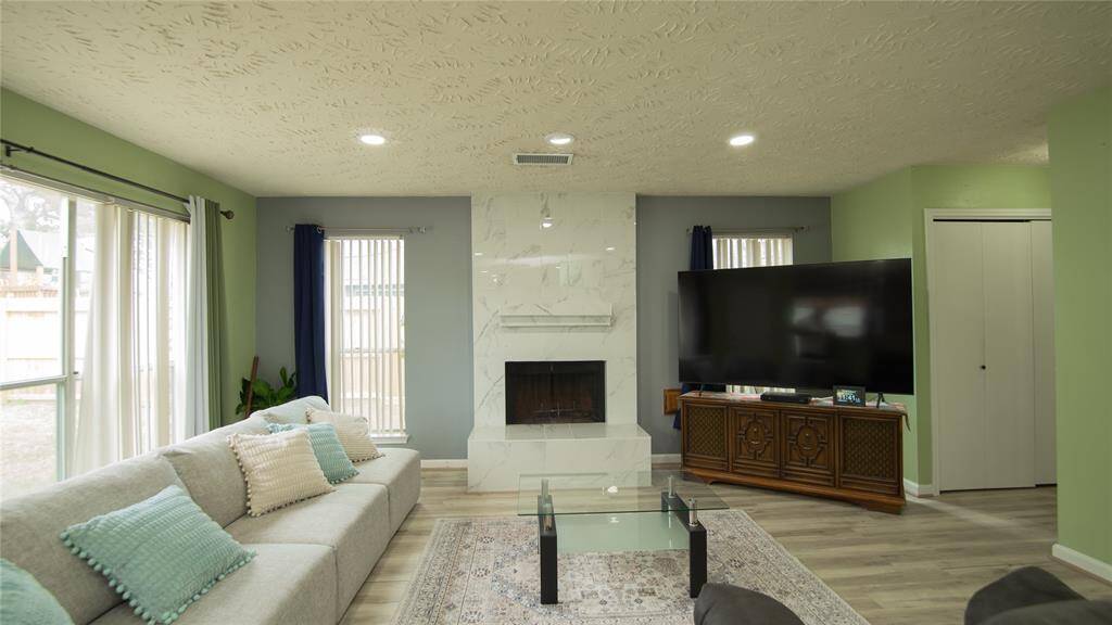 This living room features a modern design with a cozy fireplace and ample natural light. It has a neutral color palette, providing a welcoming space for relaxation.