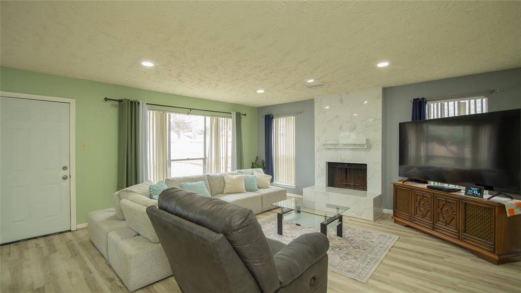 This living room features a modern design with a cozy fireplace and ample natural light. It has a neutral color palette, providing a welcoming space for relaxation.