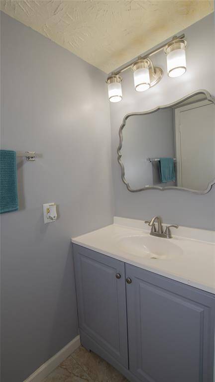 This bathroom features a modern vanity with a sleek sink, stylish mirror, and contemporary lighting. The soft gray walls and cabinetry create a calming atmosphere, complemented by a marble-patterned floor and a convenient towel rack.