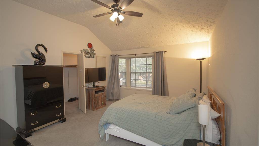 The primary bedroom features a high ceiling with a ceiling fan, ample natural light from a large window, walk-in closet, and neutral painted walls.