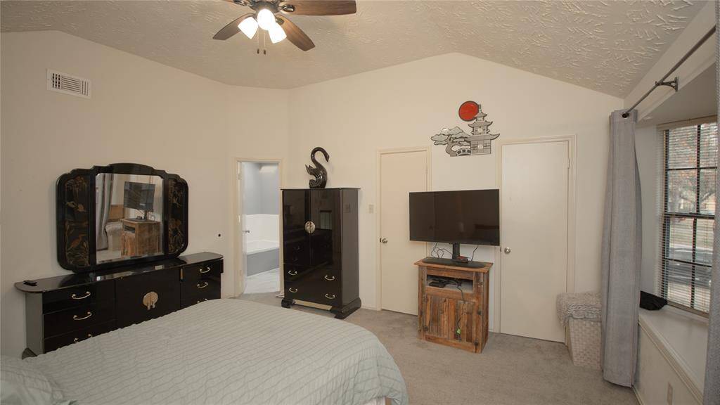 The primary bedroom features a high ceiling with a ceiling fan, ample natural light from a large window, walk-in closet, and neutral painted walls.