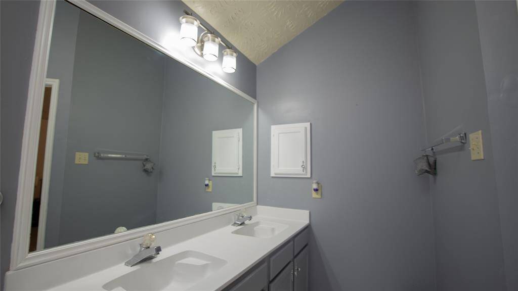 The primary bathroom features a dual-sink vanity with a large mirror and modern lighting. The walls are painted in a neutral tone, providing a clean and spacious feel.