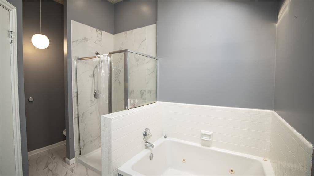 The primary bathroom features a modern design with gray walls and a seamless blend of a glass-enclosed shower, sky light, and jetted bathtub, offering a clean and stylish look.