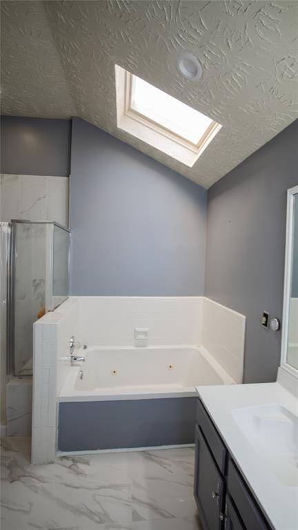 This bathroom features a large jetted tub beneath a skylight, providing natural light. It has modern gray walls, a glass-enclosed shower, and sleek cabinetry with a marble-style floor.