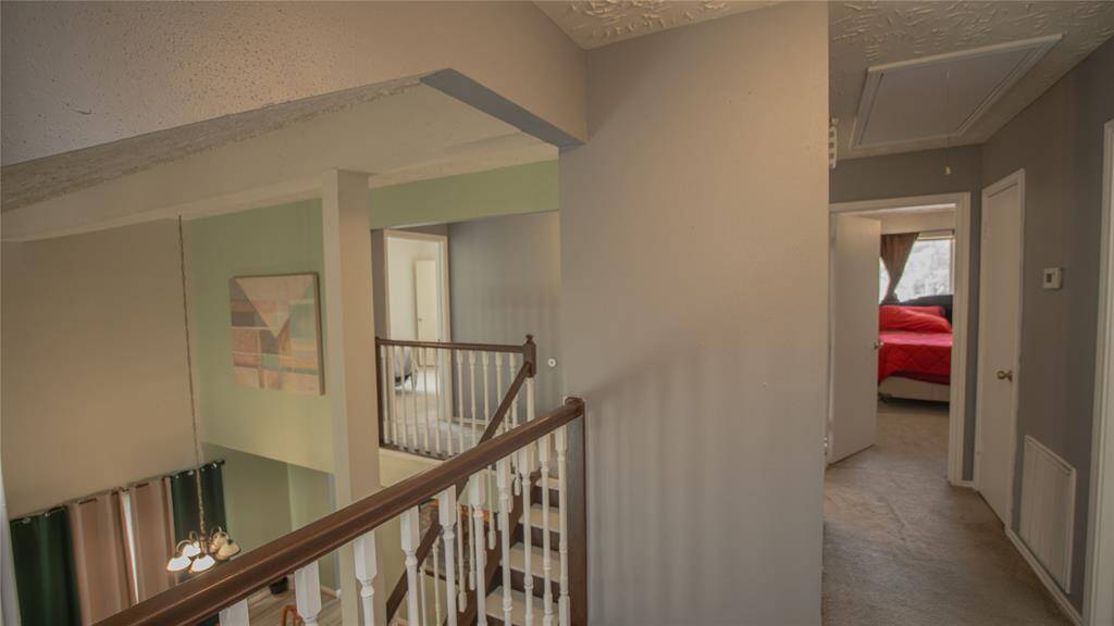 The upstairs hallway allows access to all of the bedrooms and secondary bathroom. The staircase is composed of a wooden railing with white spindles. The space feels open with natural light coming in.