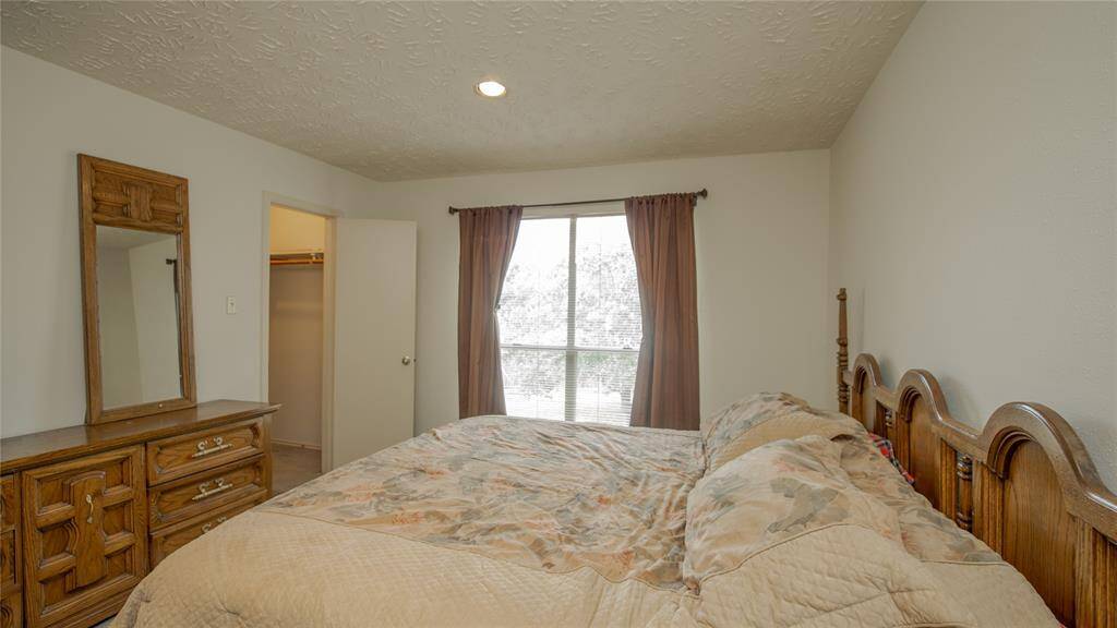 Cozy bedroom with natural light from a large window, featuring a classic wooden bed and dresser. The room includes a small closet and is painted in a neutral tone, offering a warm and inviting atmosphere.