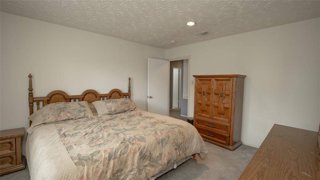 Cozy bedroom with natural light from a large window, featuring a classic wooden bed and dresser. The room includes a small closet and is painted in a neutral tone, offering a warm and inviting atmosphere.