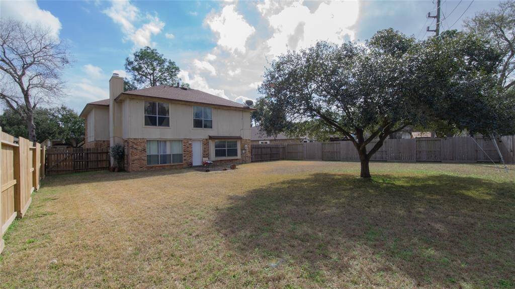 Spacious backyard with a large tree providing shade, surrounded by a wooden fence for privacy. Suitable for outdoor activities or gardening.
