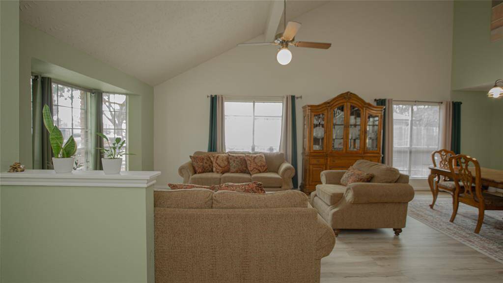 This spacious living room features high ceilings, soft green walls, and ample natural light. Plenty of space for comfortable seating.