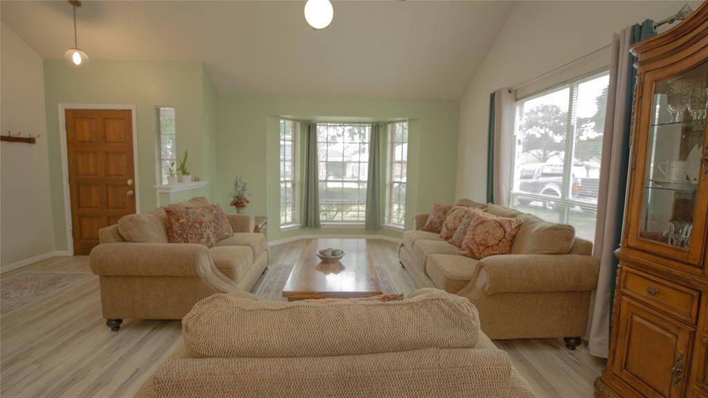 Bright and inviting living room with large windows, neutral walls, and light wood flooring. Features comfortable seating, a wooden coffee table, and a cozy atmosphere, perfect for relaxation and family gatherings.