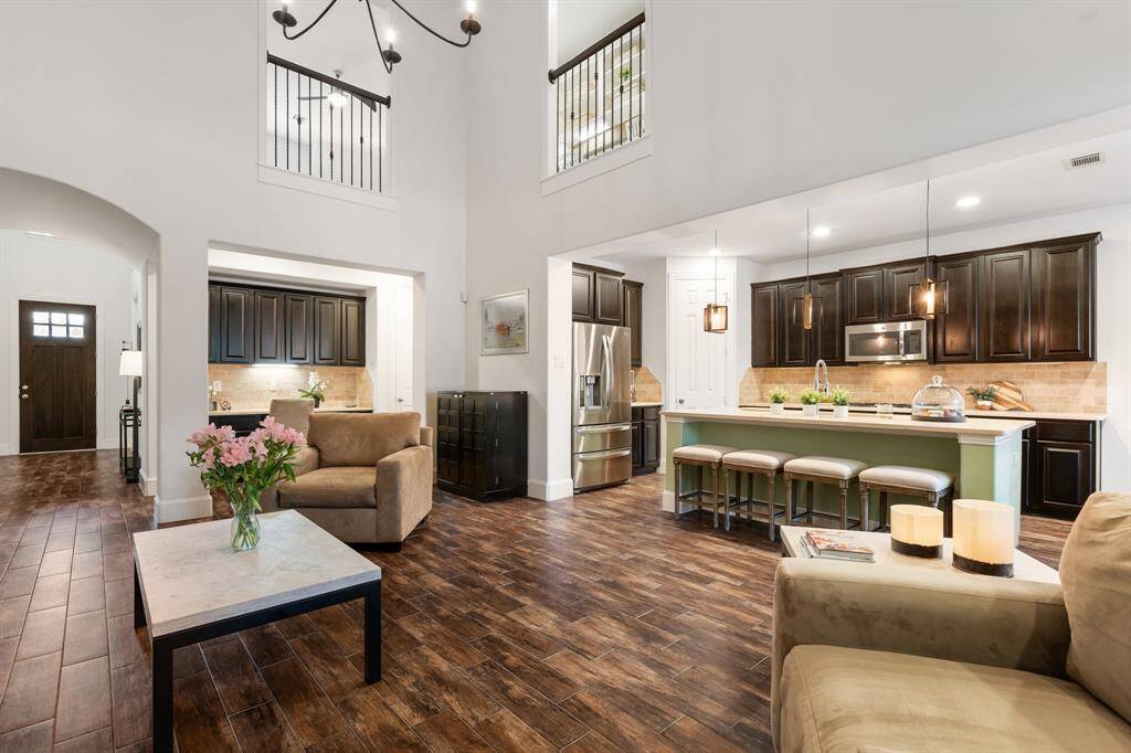 This spacious open-concept living area features high ceilings and abundant natural light. The kitchen has modern GE appliances, dark cabinetry with soft close drawers and cabines, and a large island with room for seating. Stylish wood like tile flooring extends throughout, creating a warm and inviting atmosphere.