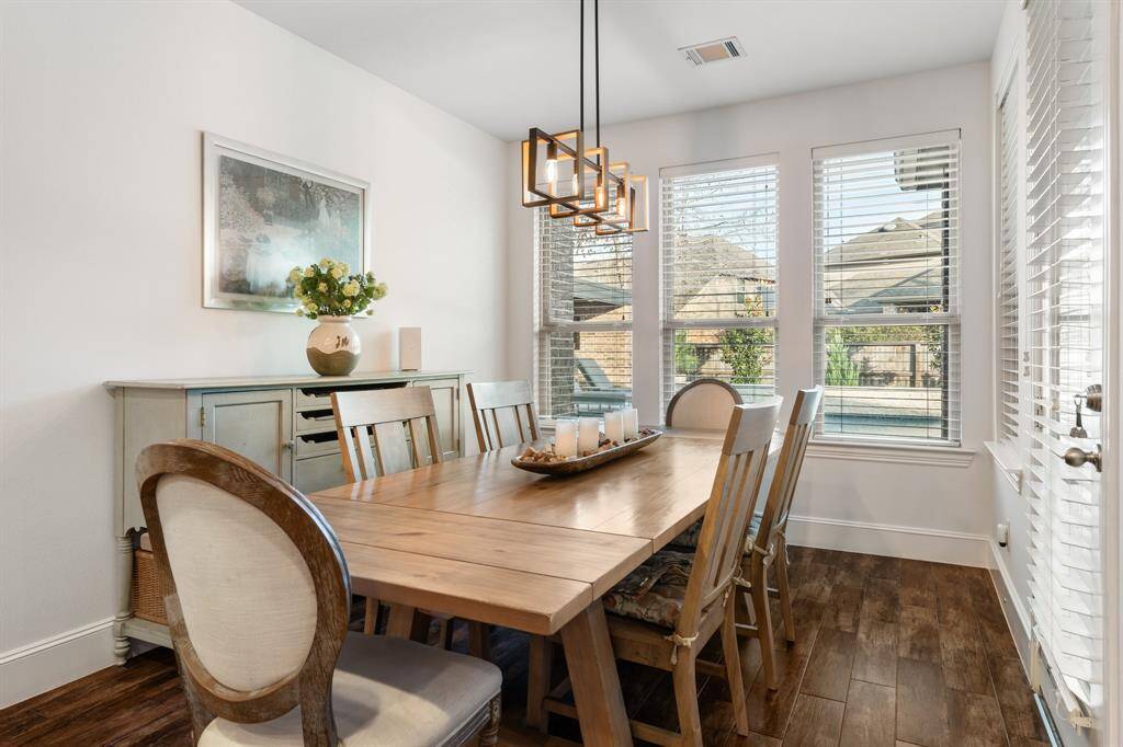This dining area is bright and inviting, featuring large windows that provide plenty of natural light, and the room is accented by a modern, stylish light fixture. The hardwood like tile floor adds warmth, and tall baseboards create and elegant luxurious touch to the walls.
