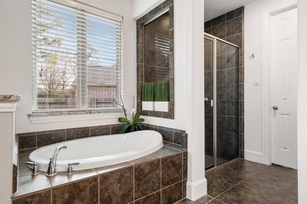 This bathroom features a spacious soaking tub with a tile surround, a separate glass-enclosed shower, and a large window for natural light. The neutral tones and modern fixtures create a relaxing atmosphere.