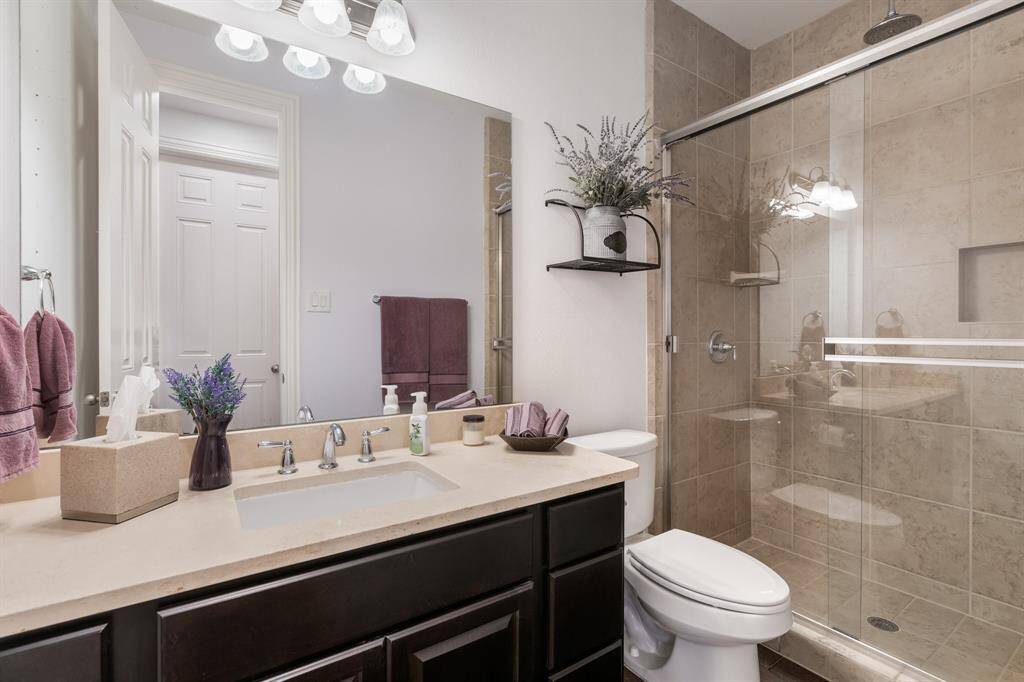 This bathroom features a modern design with a spacious glass-enclosed shower, neutral tile walls, and a sleek vanity with a wide mirror. The countertop offers ample space, creating a welcoming and functional space. This full bath is off of the 2ndary downstairs bedroom, kitchen, breakfast and living area.