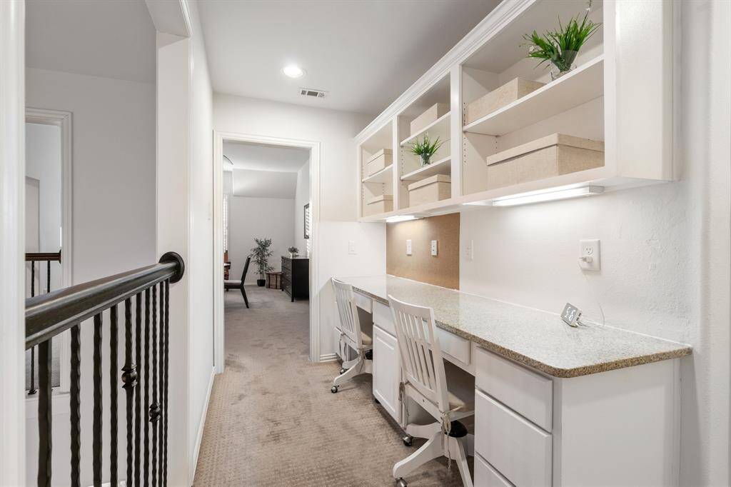 This photo features a bright, functional home office nook upstairs with built-in desks and shelving. It has a clean, organized appearance, ideal for a productive workspace. The area connects to a hallway, leading to two other bedrooms, adding convenience and accessibility.