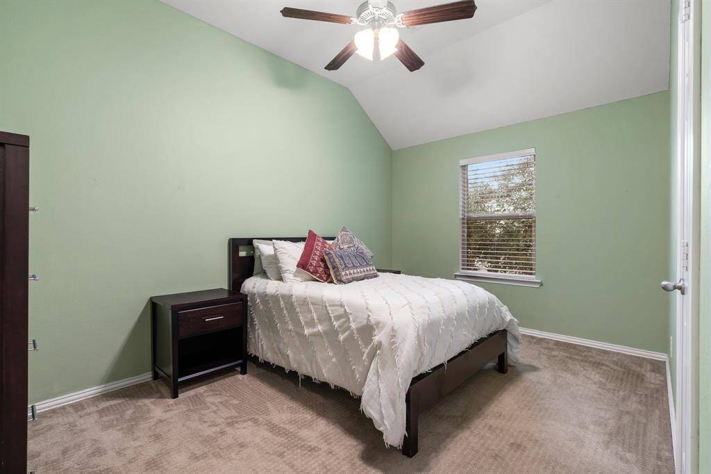 This cozy bedroom features soft green walls, a vaulted ceiling with a ceiling fan, a closet and a window providing natural light.
