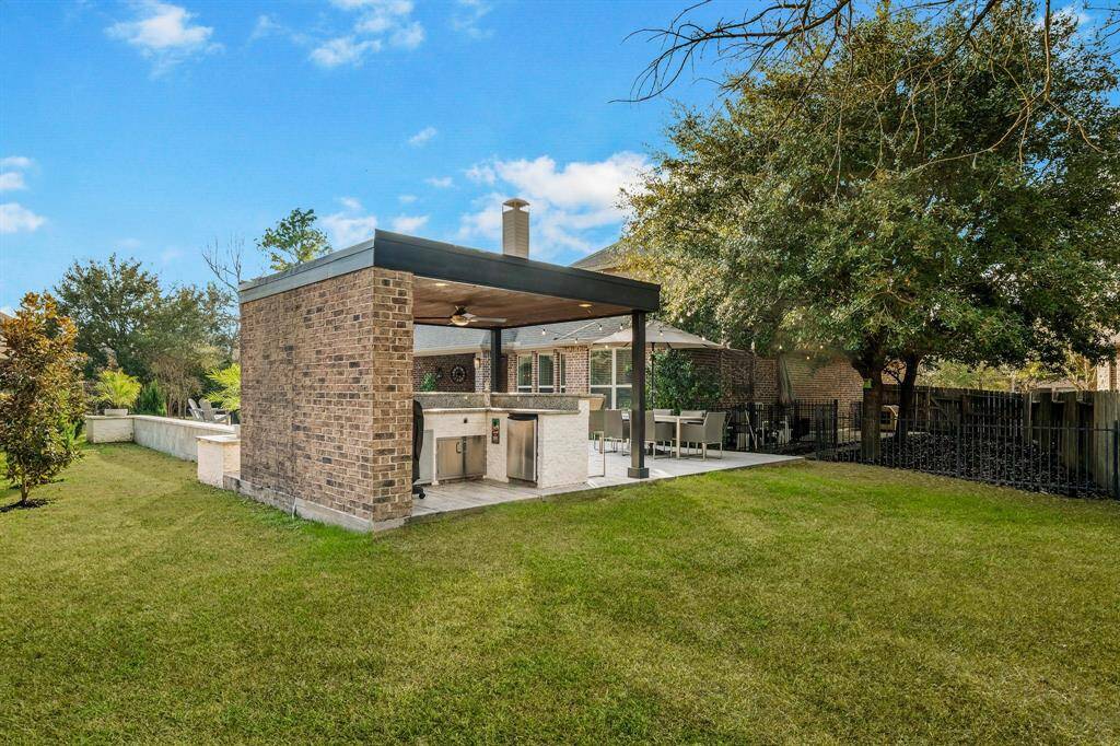 This backyard features a spacious outdoor living area with a brick structure, including a covered patio and built-in kitchen. The well-maintained lawn and mature trees offer a private and inviting space for relaxation and entertaining.