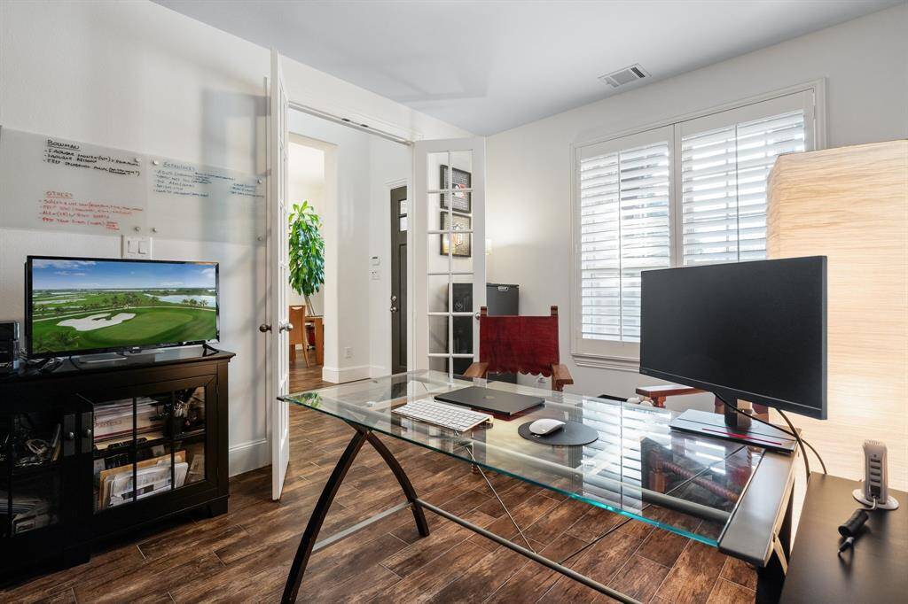 This photo showcases a stylish home office featuring accent walls that look like brick. The room is well-lit with large front windows and custom wood plantation shutters and has a modern yet cozy ambiance, perfect for productivity and relaxation.