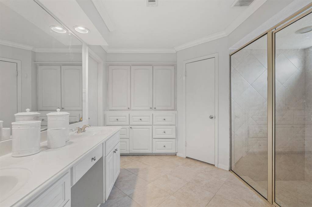 Large Primary Bathroom with built-in cabinetry features a tiled walk-in shower, double sinks and vanity with tile floor.