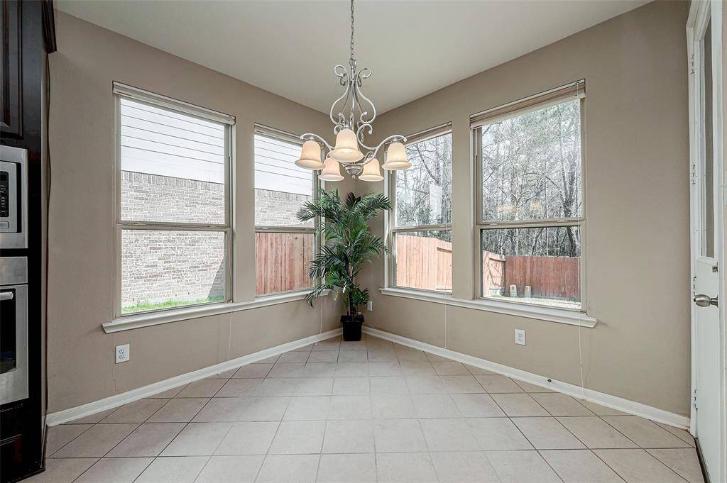 Bright breakfast nook with large windows, tiled flooring. It offers a cozy space with views of the fenced backyard, perfect for morning meals or casual dining.