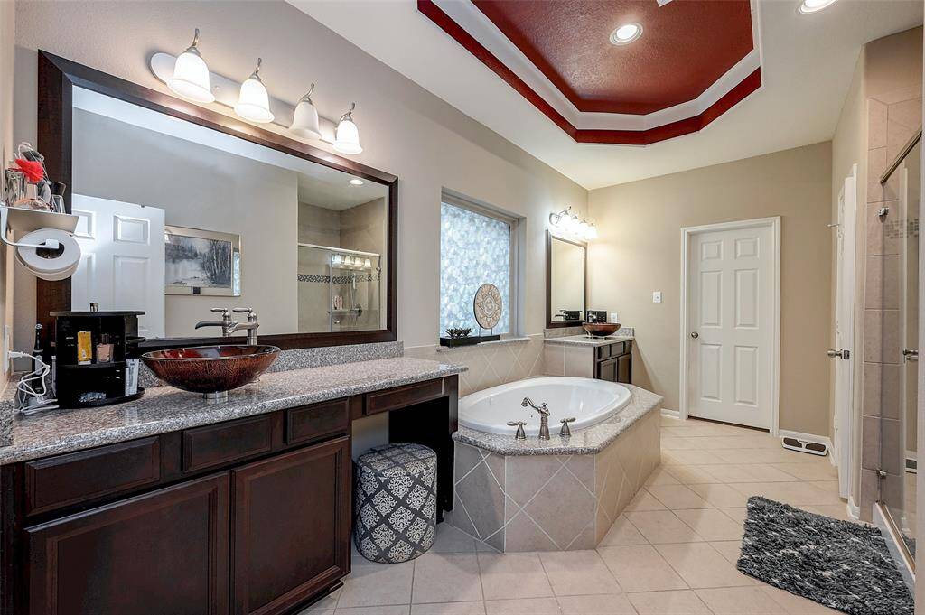Primary bathroom features a spacious design with a spa-like bathroom, dual vessel sinks on granite countertops, and a large mirror. It has a modern aesthetic with recessed lighting, a separate shower, and a decorative ceiling. The neutral tones create a relaxing atmosphere.