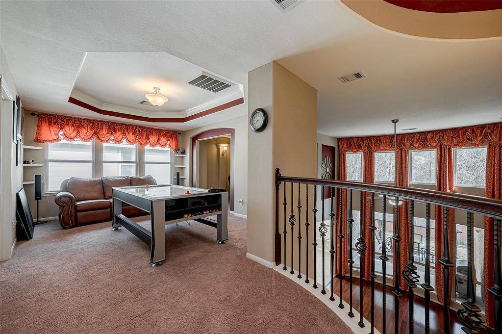 Upstairs entertainment area featuring a game table. Large windows with red curtains provide ample natural light. The space overlooks a high-ceilinged living area with an elegant railing