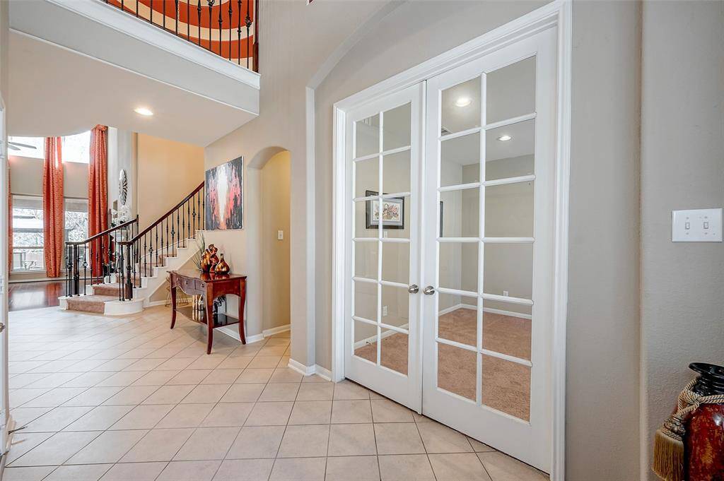Spacious foyer with tiled flooring, a beautiful wrought iron staircase, and elegant French doors leading to a bright office and living area. Two story high ceilings and large windows throughout, provides abundant natural light, creating a welcoming atmosphere.