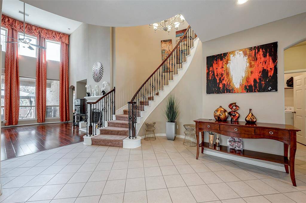 A grand entryway with a curved staircase, high ceilings, and large windows. The space features elegant tile and hardwood flooring, modern artwork, and stylish decor, creating a welcoming and sophisticated atmosphere.