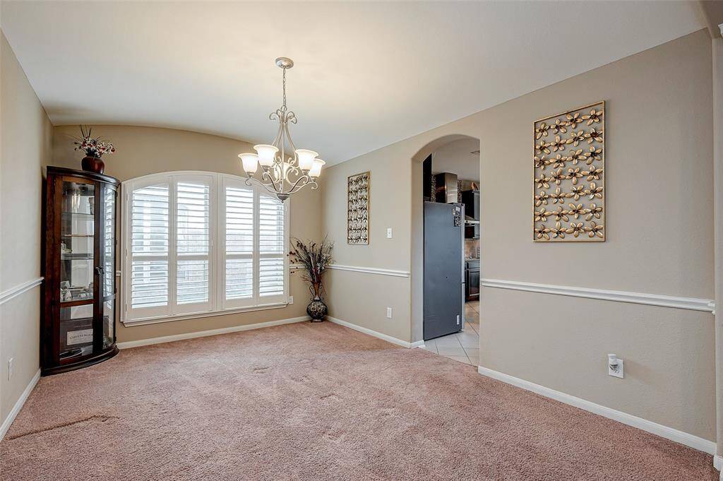 Formal dining area featuring a large window with shutters and elegant chandelier lighting. Decorative wall accents and a corner display cabinet add character. Opens to the kitchen through an arched doorway.